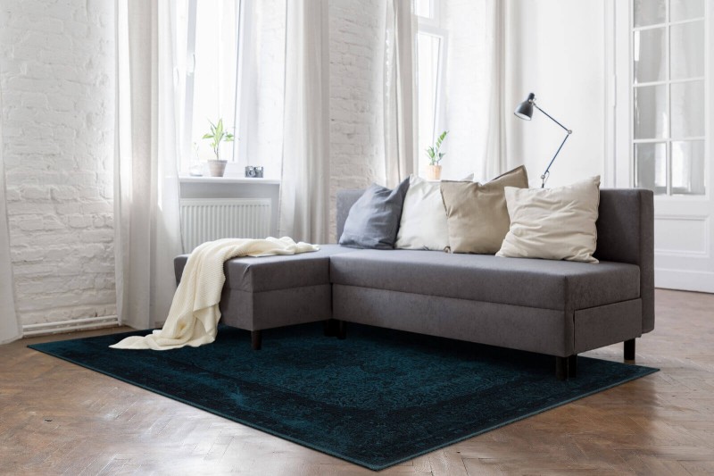 Dywan wełniany Agnella Agnus Tobe szmaragd w salonie na tle szarej kanapy i białych ścian