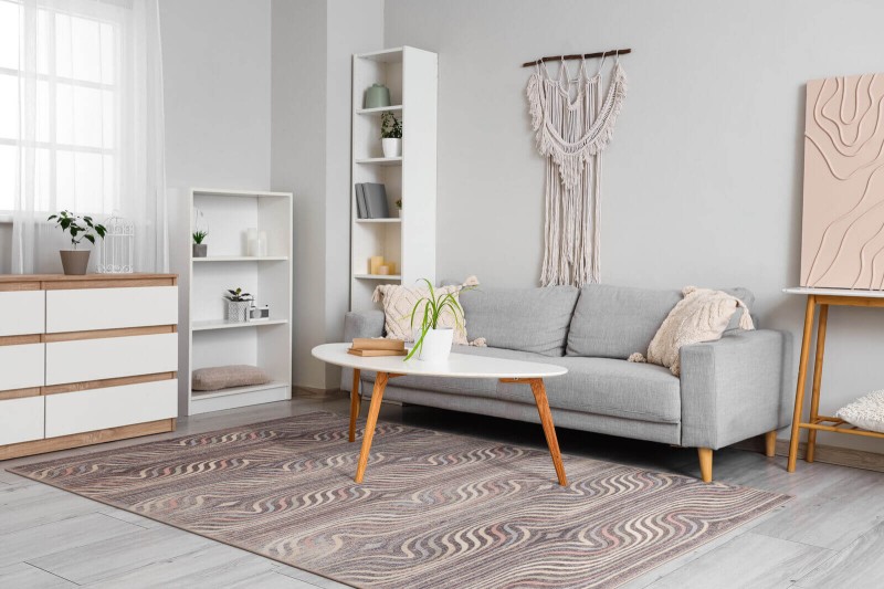 Dywan wełniany nowoczesny Agnella Isfahan Sewilla w kolorze wrzosowym w pokoju dziennym na tle szarej kanapy
