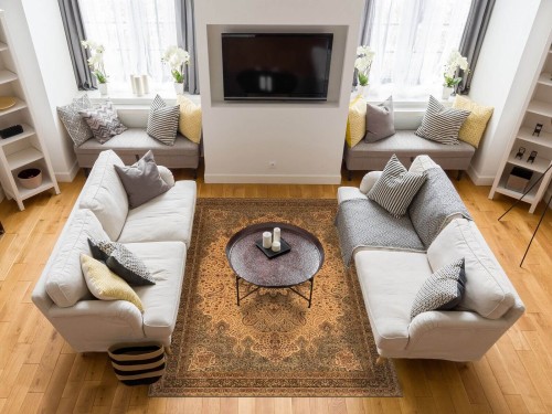 Dywan wełniany Agnella Agnus Namak kolor oliwka w przytulnym salonie z szarymi kanapami i kominkiem