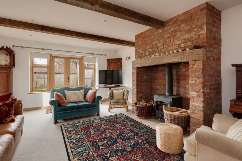 Dywan wełniany Agnella Isfahan Hela w kolorze granatowym w salonie w stylu rustykalnym z kominkiem z cegły