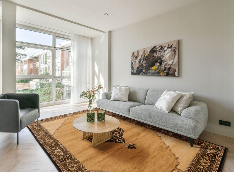 Dywan wełniany klasyczny Agnella Isfahan Uriasz kolor sahara w nowoczesnym salonie z szarą kanapą i dużym oknem