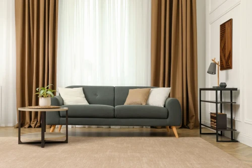 Dywan wełniany Agnella Ballata Alova w kolorze beżowym w salonie z grafitową kanapą i ciemnobeżowymi zasłonami