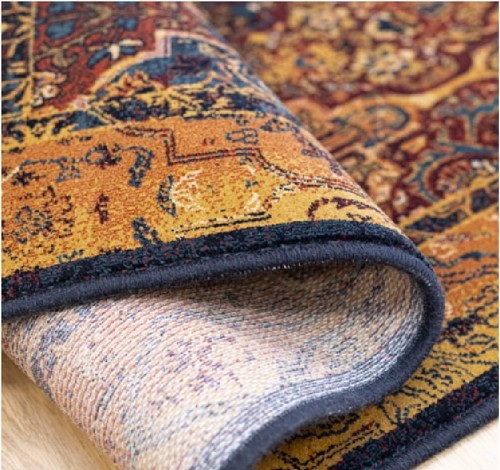 Fragment zwiniętego dywanu z widocznym obszyciem i spodem dywanu Dywilan Superior Kain miedź