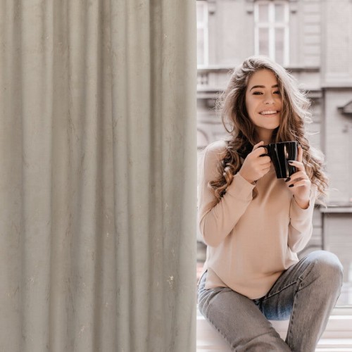 Kobieta przy zasłonie z welwetu 140x300 cm na taśmie Nadia beżowo-złota