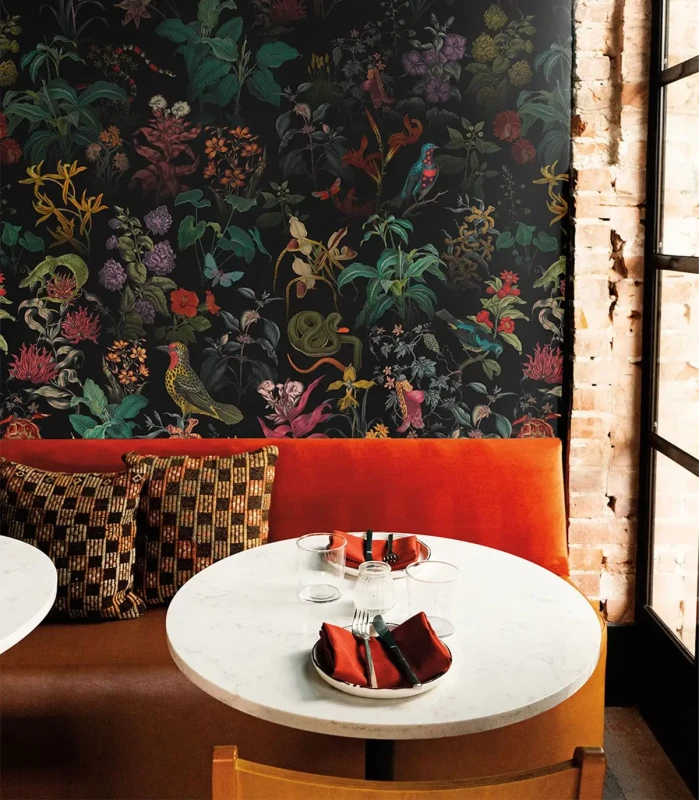 Restauracyjny kącik z czerwoną kanapą i białym stolikiem na tle czarnej tapety w egzotyczne rośliny i zwierzęta Garden Ombre.webp