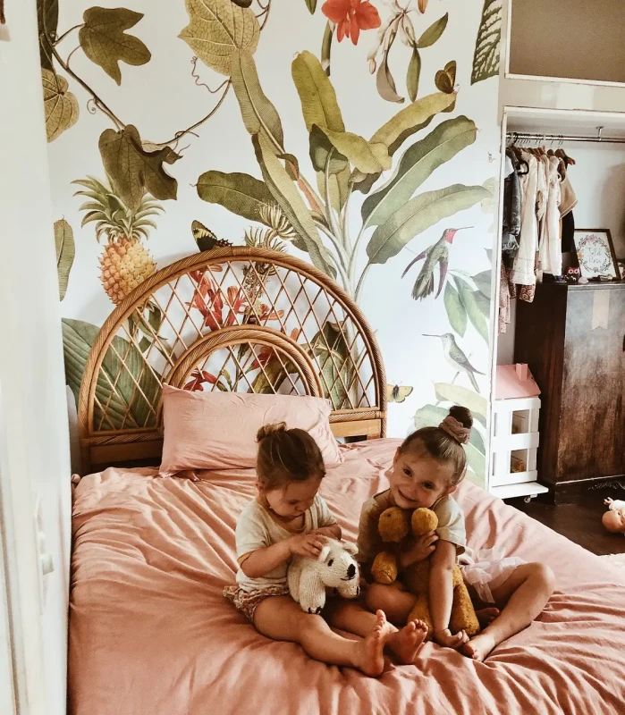Mural dziecięcy Tropicana na ścianie w pokoju z łóżkiem i wesołymi dziewczynkami.webp