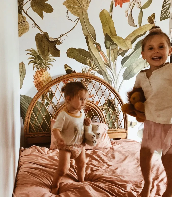 Małe dziewczynki na łóżku na tle tapety Tropicana.webp