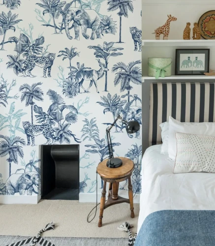 Tapeta z niebieskimi rysunkami dzikich zwierząt i tropikalnej roślinności we wnętrzu z łóżkiem i dekoracjami safari