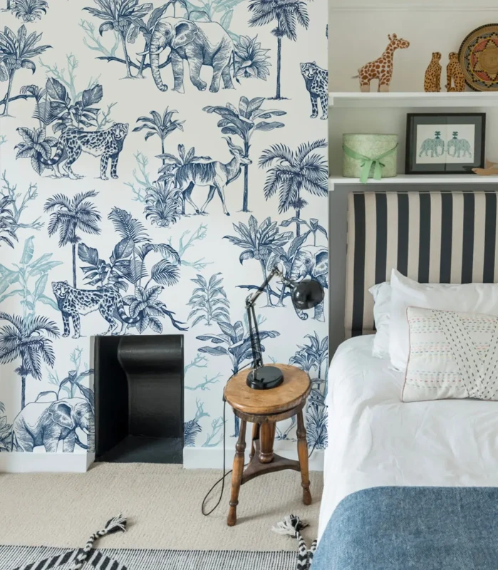 Tapeta z niebieskimi rysunkami dzikich zwierząt i tropikalnej roślinności we wnętrzu z łóżkiem i dekoracjami safari