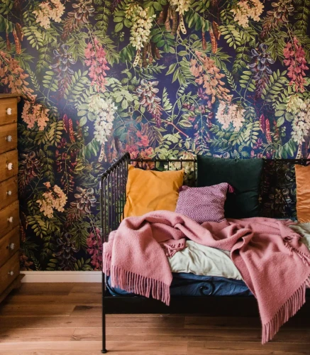 Tapeta w kwiaty Acacia Dark Blue za metalowym łóżkiem z poduszkami.webp